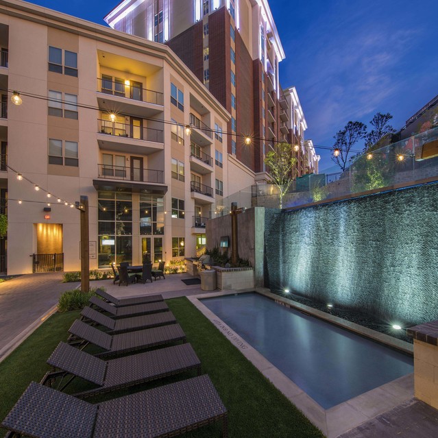 The Arcadian - Apartment Building at Twilight, Featuring a Serene Poolside Area with Lounge Chairs and an Illuminated Wall