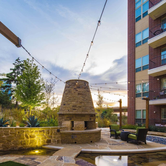The Arcadian - Outdoor Lounge Area Featuring a Stone Fireplace, Cozy Seating, and String Lights Against a Sunset Sky