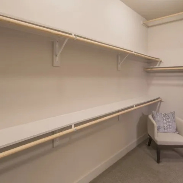 The Arcadian - Spacious Walk-in Closet with Light-Colored Walls, Long Shelves, and a Chair in the Corner