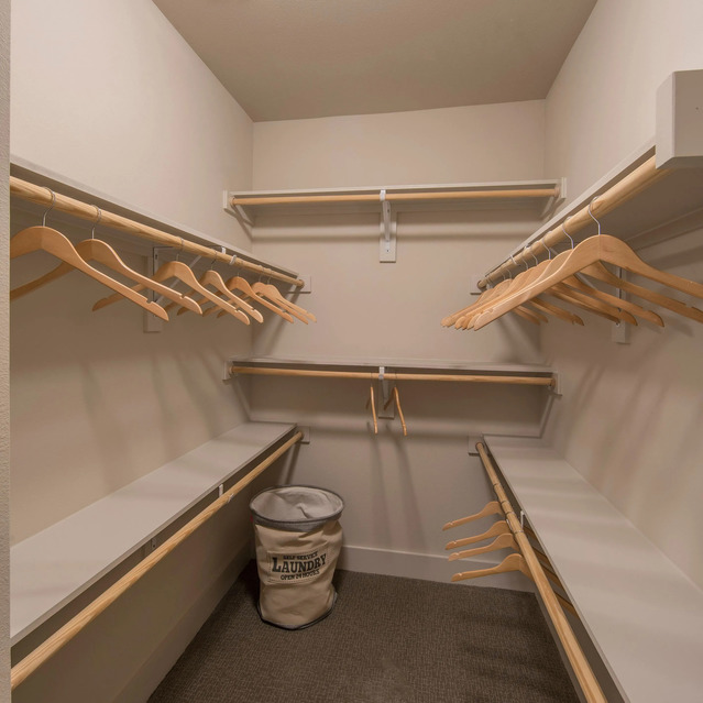 The Arcadian - Spacious Closet Featuring Wooden Hangers, Shelves, and a Laundry Basket on a Carpeted Floor