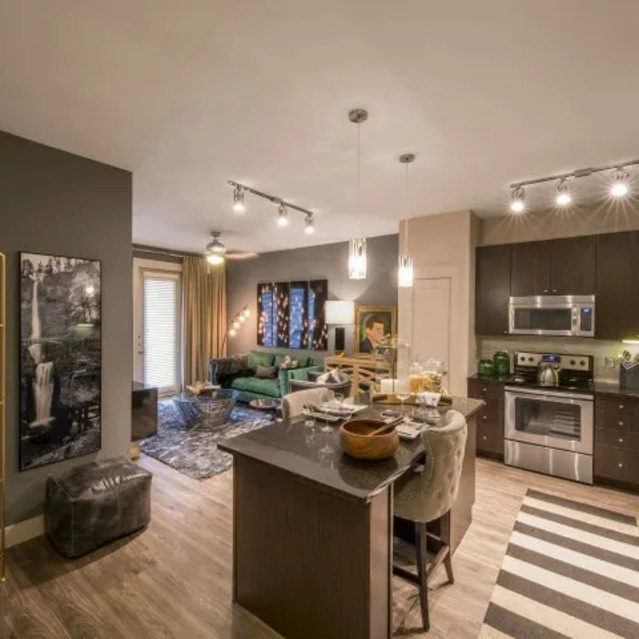 The Arcadian - Open-Plan Kitchen and Living Room with Warm Lighting, Dark Wood Cabinets, a Central Island, and a Striped Rug