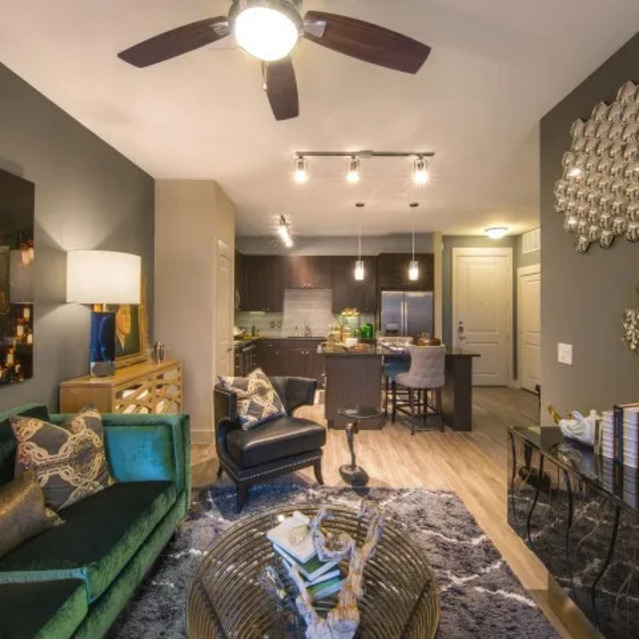 The Arcadian - Stylish Living Room with a Green Velvet Sofa, Gold Accents, Mirrored Wall Art, and Modern Lighting